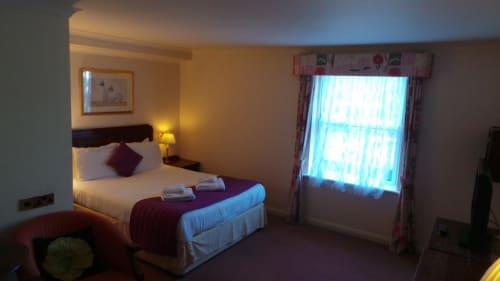 Chambre Double Classique de l'Hôtel La Trelade avec lit aux accents bordeaux, éclairage chaleureux et grande fenêtre drapée