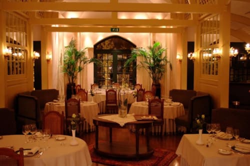 Élégante salle à manger du Château d'Hassonville avec tables rondes, chaises capitonnées, éclairage chaleureux et plantes décoratives