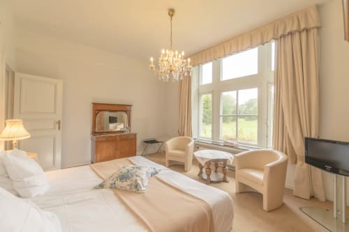 Elegant slaapkamer in Château d'Hassonville met kroonluchter, antiek meubilair en tuinzicht in Marche-en-Famenne.