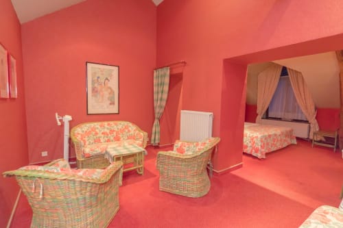 Helder koraalkleurige slaapkamer in Château d'Hassonville B&B in Marche-en-Famenne met rotan meubels en bloemenpatroon kussens