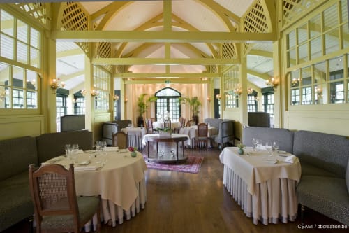 Élégante salle à manger du Château d'Hassonville à Marche-en-Famenne avec poutres en bois jaune, tables rondes et lumière naturelle