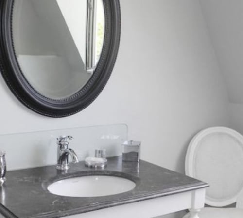 Modern bathroom vanity with dark countertop, white sink, chrome faucet, and round mirror at Le château d'Hermonville
