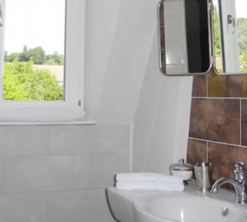 Modern bathroom with white tiles, sink, mirror, and vineyard views at Le château d'Hermonville