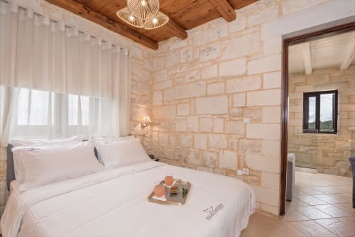Modern bedroom at Villa Freedom with stone walls, wooden beams, and en-suite bathroom in Kokkino Chorio, Crete