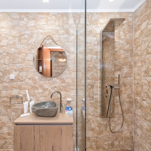 Modern bathroom at Villa Freedom with stone-tiled walls, vessel sink, round mirror, and walk-in shower in Crete