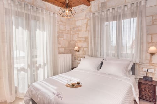 Elegant bedroom at Villa Freedom B&B in Crete with white bedding, stone walls, sheer curtains, and warm lighting