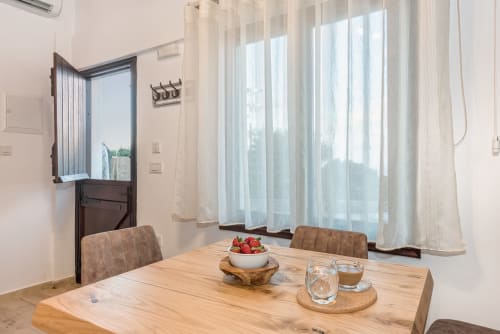 Bright dining area at Villa Freedom in Crete with wooden table, sheer curtains, fresh strawberries, and open door to balcony