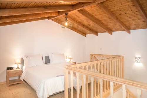 Spacious bedroom at Villa Freedom with wooden ceiling beams, king bed, and wooden railing overlooking mezzanine in Crete