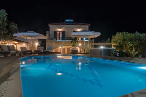 Villa Freedom pool at night in Kokkino Chorio, Crete with illuminated water, loungers and stone building