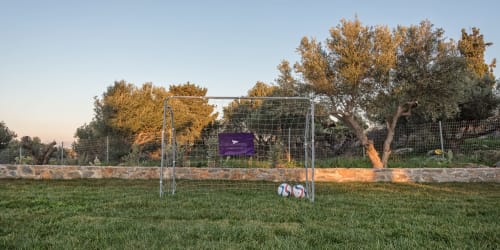 Soccer goal with balls on grass at Villa Freedom, Crete, with autumn trees and stone wall backdrop
