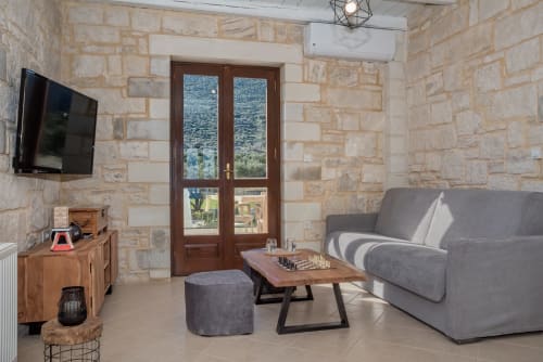 Modern living room at Villa Freedom in Kokkino Chorio, Crete with stone walls, gray sofa, and sea views
