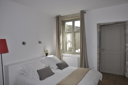 Bright double bedroom at Le Jardin De Beauvoir in Lyon with white bedding, grey accents, and French doors overlooking the