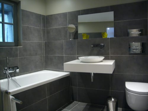 Modern dark-tiled bathroom at Le Jardin De Beauvoir Lyon with white vessel sink, bathtub and toilet