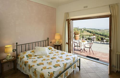 Camera doppia con biancheria gialla a fiori e terrazza con vista sul paesaggio toscano presso B&B I Coppi, San Gimignano