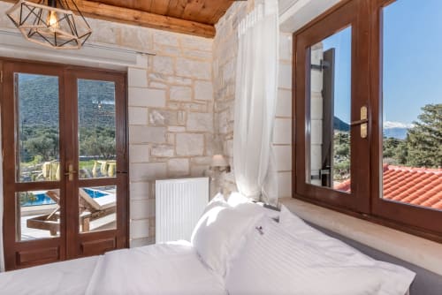 Bright bedroom at Villa Freedom in Crete with stone walls, wooden doors, mountain views, and pool access