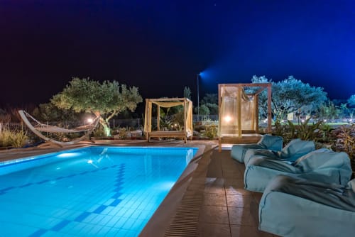 Illuminated poolside at Villa Freedom in Crete with lounge chairs, wooden pergolas, and olive trees at night