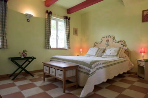 Bright bedroom at Au Petit Tambour D'Autingues with yellow walls, red beams, floral headboard, and checkered floor in