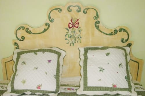 Decorative headboard with green scrollwork and mistletoe design above white pillows with green trim at Au Petit Tambour