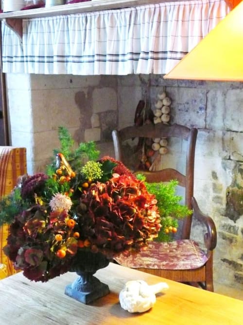 Rustic dining area at Au Petit Tambour D'Autingues with vibrant autumn floral arrangement featuring red dahlias and orange