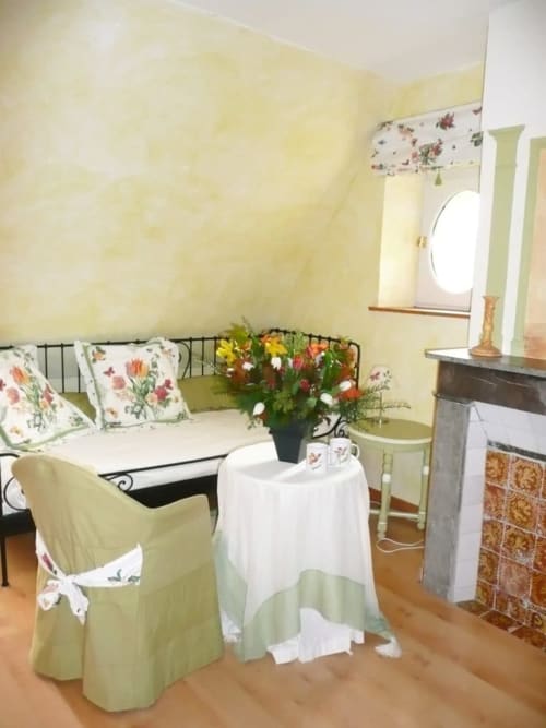 Cozy Flandre Room at Au Petit Tambour D'Autingues with floral bed, round window, and sitting area with white table and