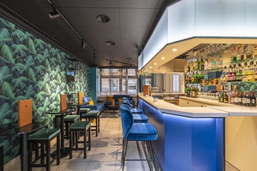 Modern hotel bar at Residence Europe & Spa in Clichy with tropical wallpaper, blue seating, and well-stocked shelving