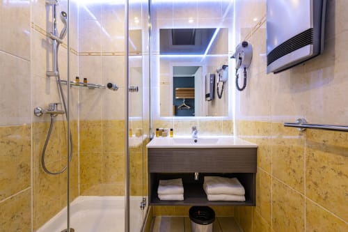 Modern bathroom at Hotel Residence Europe & Spa in Clichy with walk-in shower, illuminated mirror, and dark wood vanity
