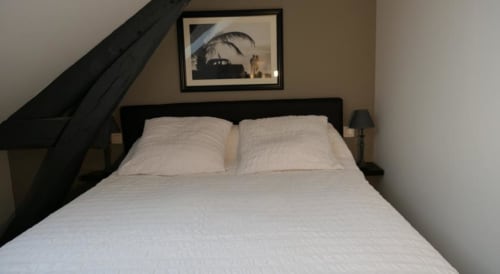 Chambre douillette sous les toits à La Maison Virginie à Montargis avec lit à structure noire, draps blancs et tableaux encadrés au-dessus de la tête de lit