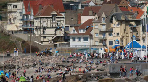 Scène animée de la plage d'Autingues avec ses bâtiments colorés, aires de jeux et visiteurs profitant du rivage de sable