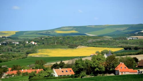 Paysage de campagne vallonnée avec des fermes traditionnelles aux toits rouges nichées parmi les champs près d'Autingues, France.
