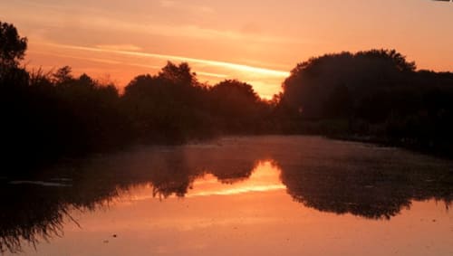Coucher de soleil doré se reflétant sur une rivière calme avec des arbres en silhouette à Au Petit Tambour D'Autingues, Autingues