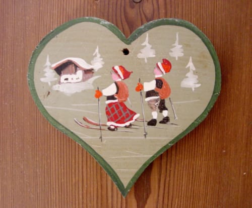 Vintage heart-shaped wooden ornament depicting children skiing in alpine winter scene at Au Petit Tambour D'Autingues,