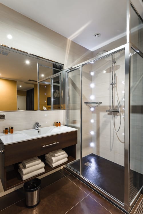 Modern bathroom at Hotel Residence Europe & Spa in Clichy with walk-in shower, white sink and dark wood vanity