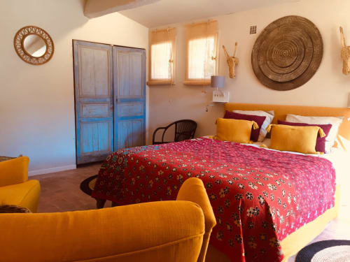 Colorful villa bedroom at Saint Martin B&B with red patterned bed, orange chairs, woven wall art, and blue wooden doors in