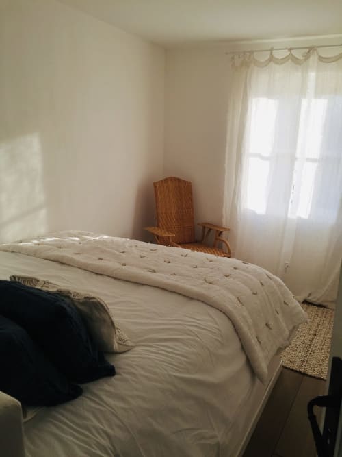 Bright bedroom at Saint Martin villa in Ollioules with cream bedding, wicker chair, and mountain views through sheer curtains