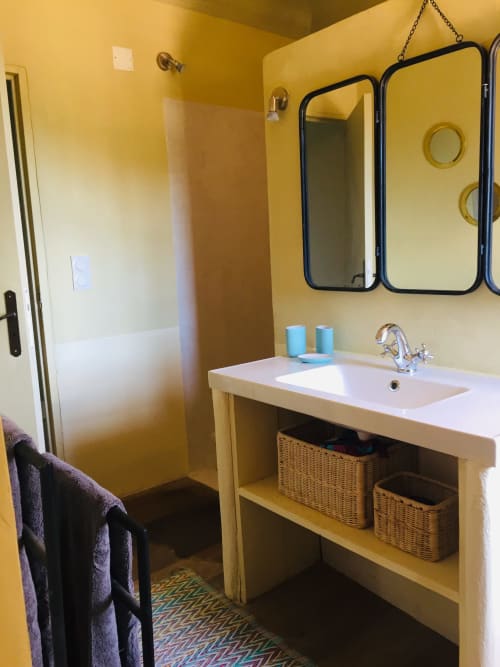 Bright yellow bathroom at Saint Martin B&B in Ollioules with white sink, black-framed mirror, shower, and wicker storage