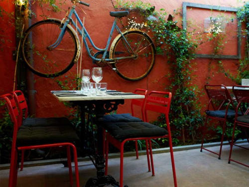 Patio de Ty Pals B&B con sillas rojas, mesita de comedor y bicicletas azules montadas en pared de terracota rodeadas de vegetación