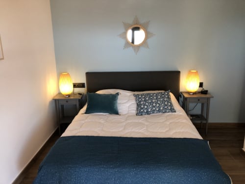 Modern bedroom at Ty Pals villa in Pals with queen bed, dark headboard, twin nightstands with warm lamps, and sunburst mirror