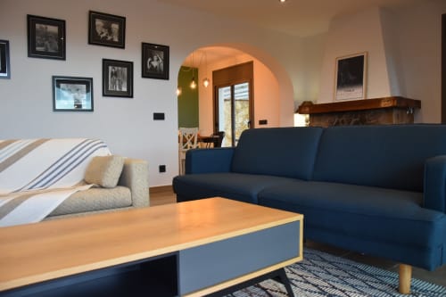 Modern living room at Ty Pals villa in Pals with blue sofa, wooden table, and sea views through arched doorway