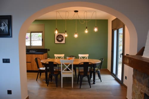 Modern dining area at Ty Pals villa in Pals with round wooden table, pendant lights, and green accent wall