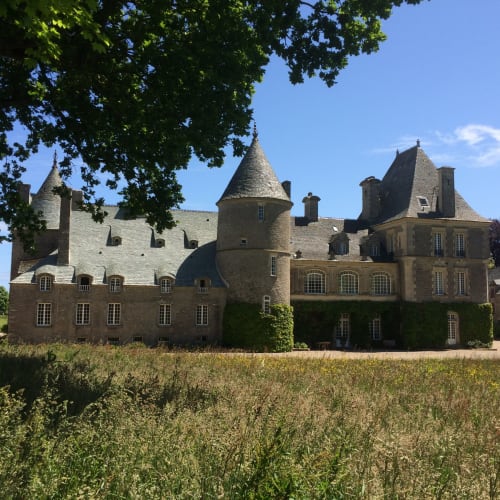 Château d'Alexis de Tocqueville, a stone castle with turrets surrounded by countryside fields in Tocqueville, France.