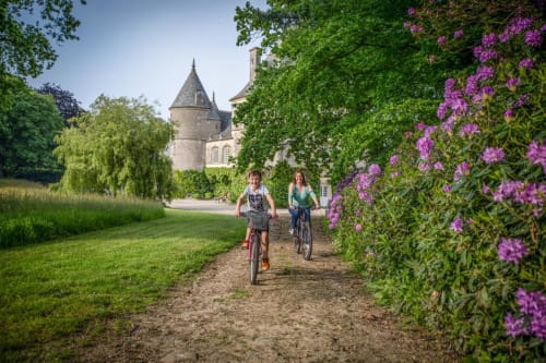Two cyclists riding through a flowering garden path toward Château d'Alexis de Tocqueville in France