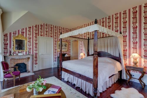 Lit à baldaquin élégant dans la luxueuse chambre du Château d'Alexis de Tocqueville avec papier peint à rayures rouges et cheminée