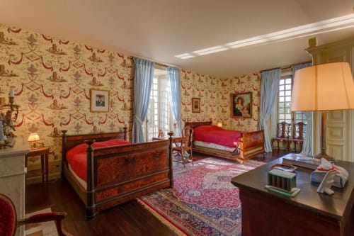 Chambre élégante du Château d'Alexis de Tocqueville avec papier peint damassé rouge, lits en bois et mobilier d'époque