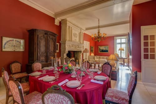 Elegant dining room at Château d'Alexis de Tocqueville with fuchsia tablecloth, ornate chairs, fireplace, and crystal