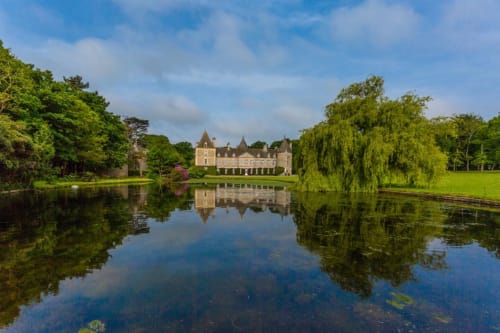 Château d'Alexis de Tocqueville reflected in peaceful water, surrounded by lush green trees and manicured grounds in