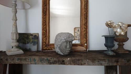 Rustic wooden mantel with decorative stone bust, ornate gold mirror, and flowers at Mas des Artistes cottage in Mouriès