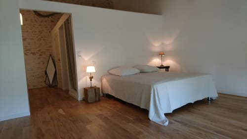 Bright bedroom in Mas des Artistes cottage with bed, white linens, bedside lamps, wooden floors and garden view