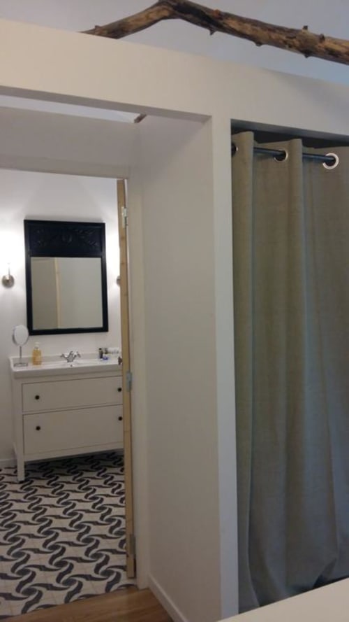 Bathroom with olive green shower curtain, white vanity, black-framed mirror, and patterned floor in Mazet 1 cottage at Mas