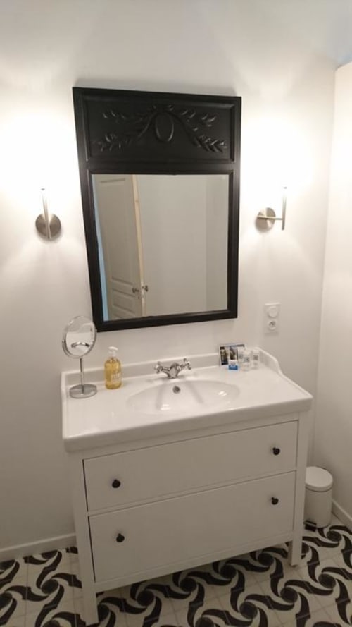 Modern bathroom vanity with white sink cabinet, black framed mirror, and decorative wall sconces at Mas des Artistes cottage