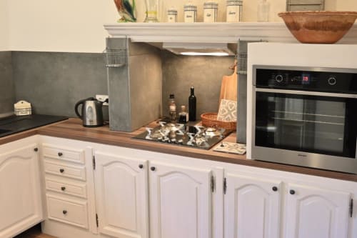 Modern kitchen in Mas des Artistes cottage with white cabinetry, wooden countertop, stainless steel oven, and open shelving